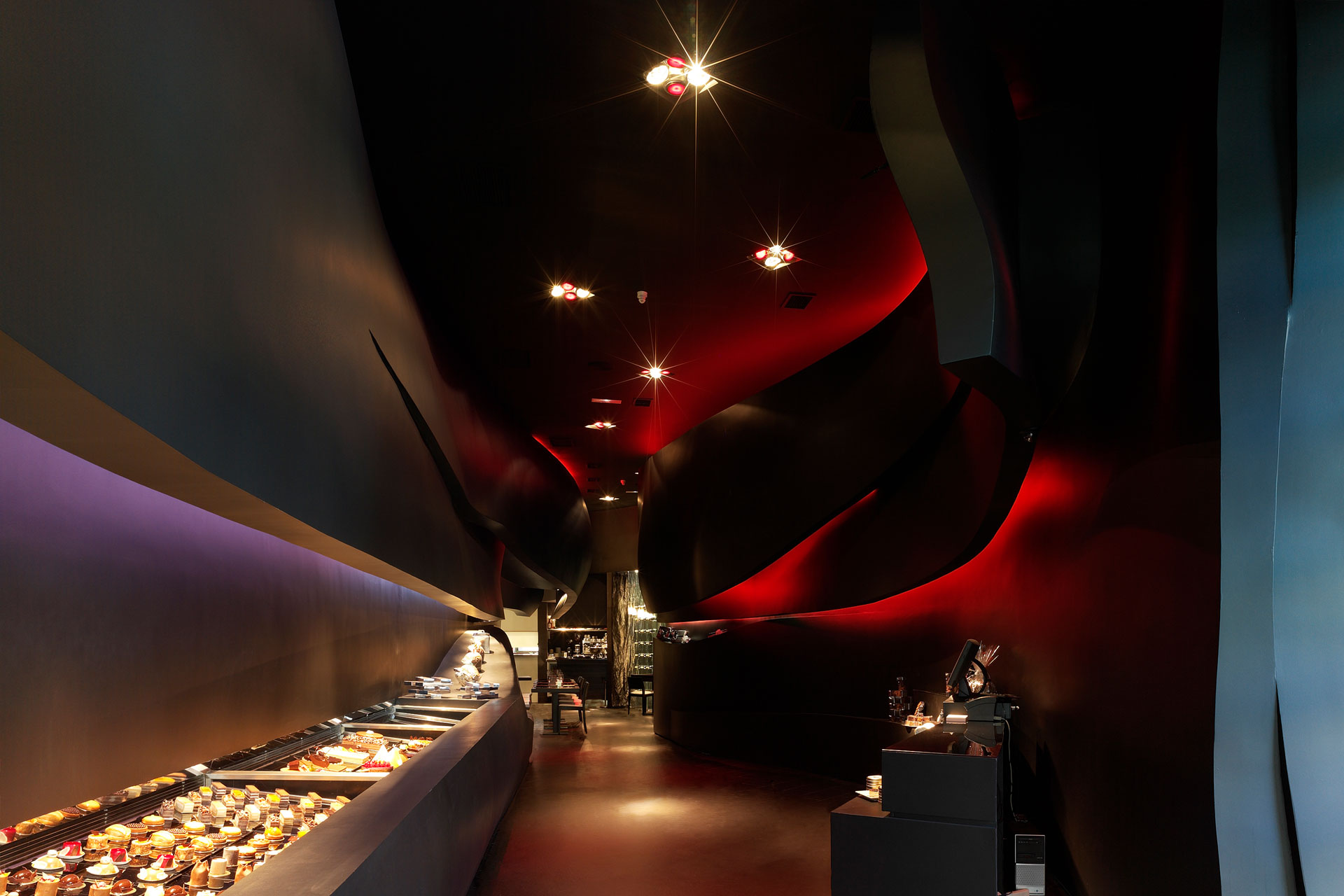 Totel Madrid con interior orgánico en rojo y negro, vitrinas iluminadas y recorrido central de la pastelería, — estudio de arquitectura Alicante tamatestudio